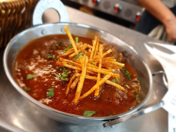 A bowl of Mallroad House Salli Boti curry topped with crispy potato straws.